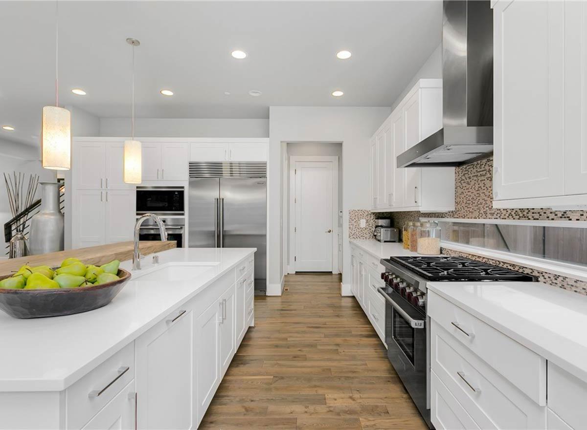 Modern kitchen with white cabinetry, large island with sink, stainless steel refrigerator, range, and vent hood.