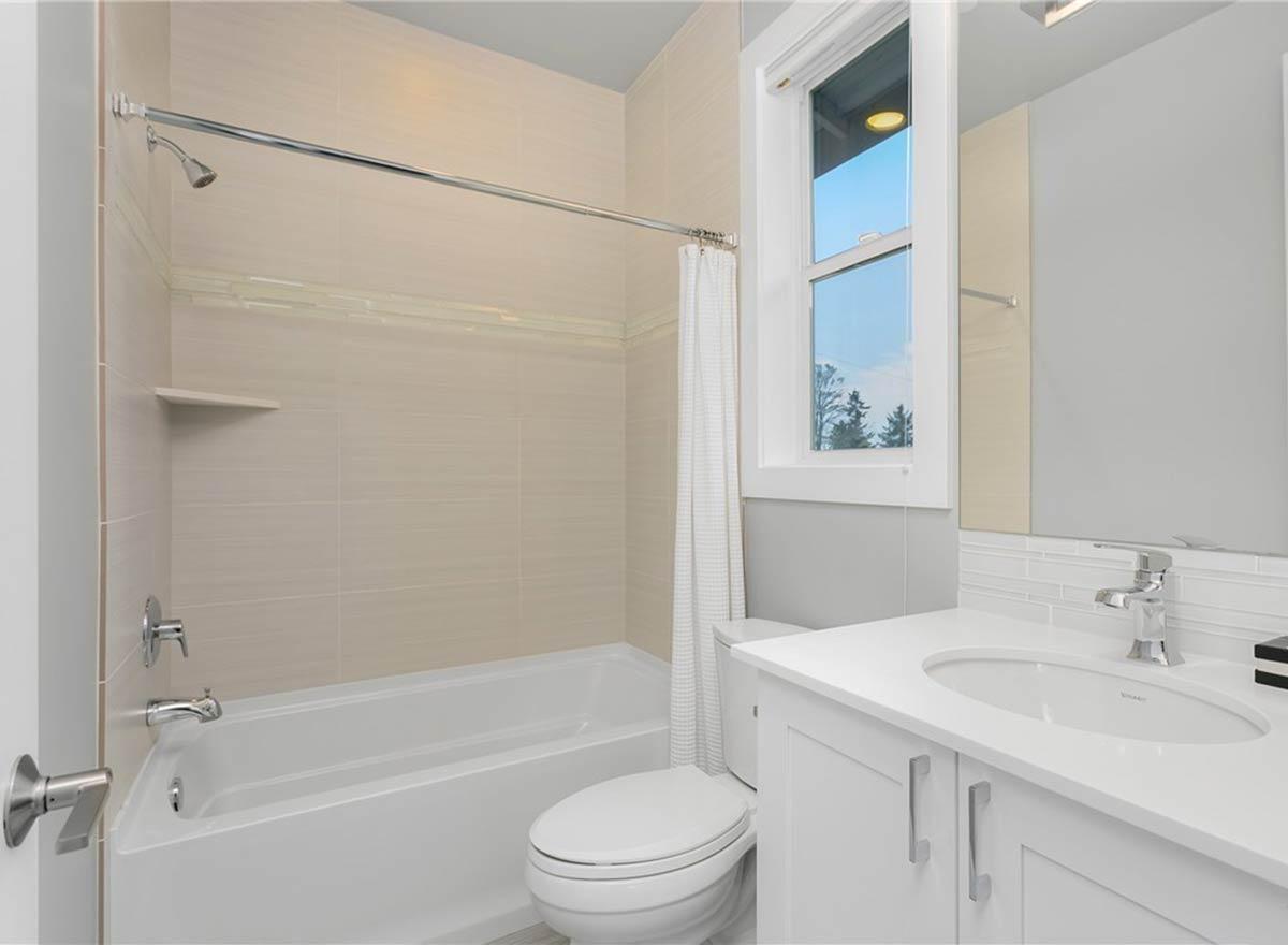 Bathroom with tiled tub/shower, toilet, vanity with sink, and window.
