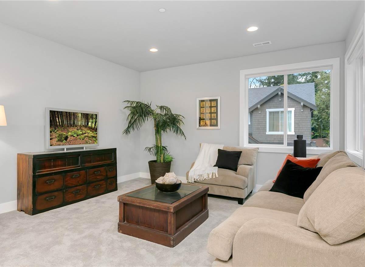Living room with tan sofa, armchair, coffee table, media console with television, and large window.