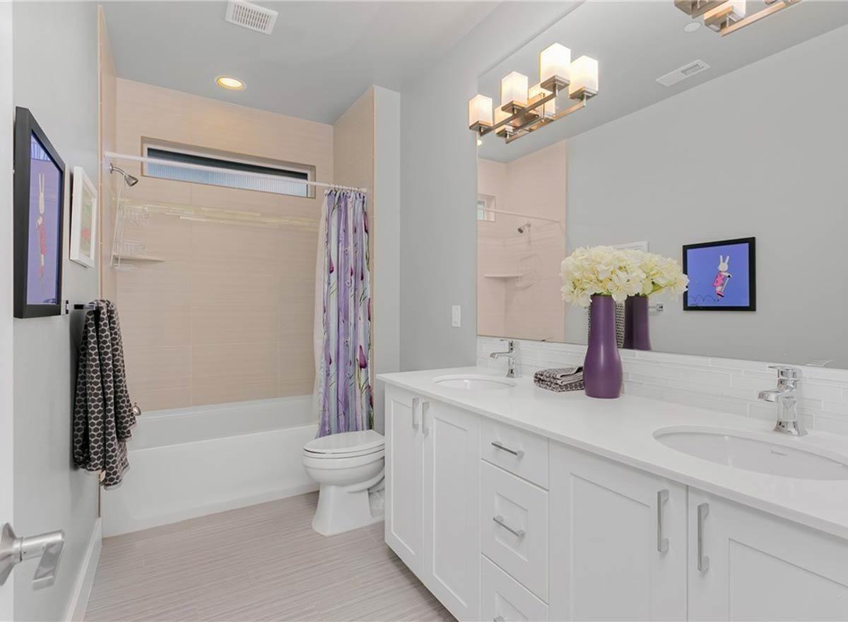 Bathroom with double vanity, white cabinets, tiled shower surround, tub, toilet, and modern light fixture.