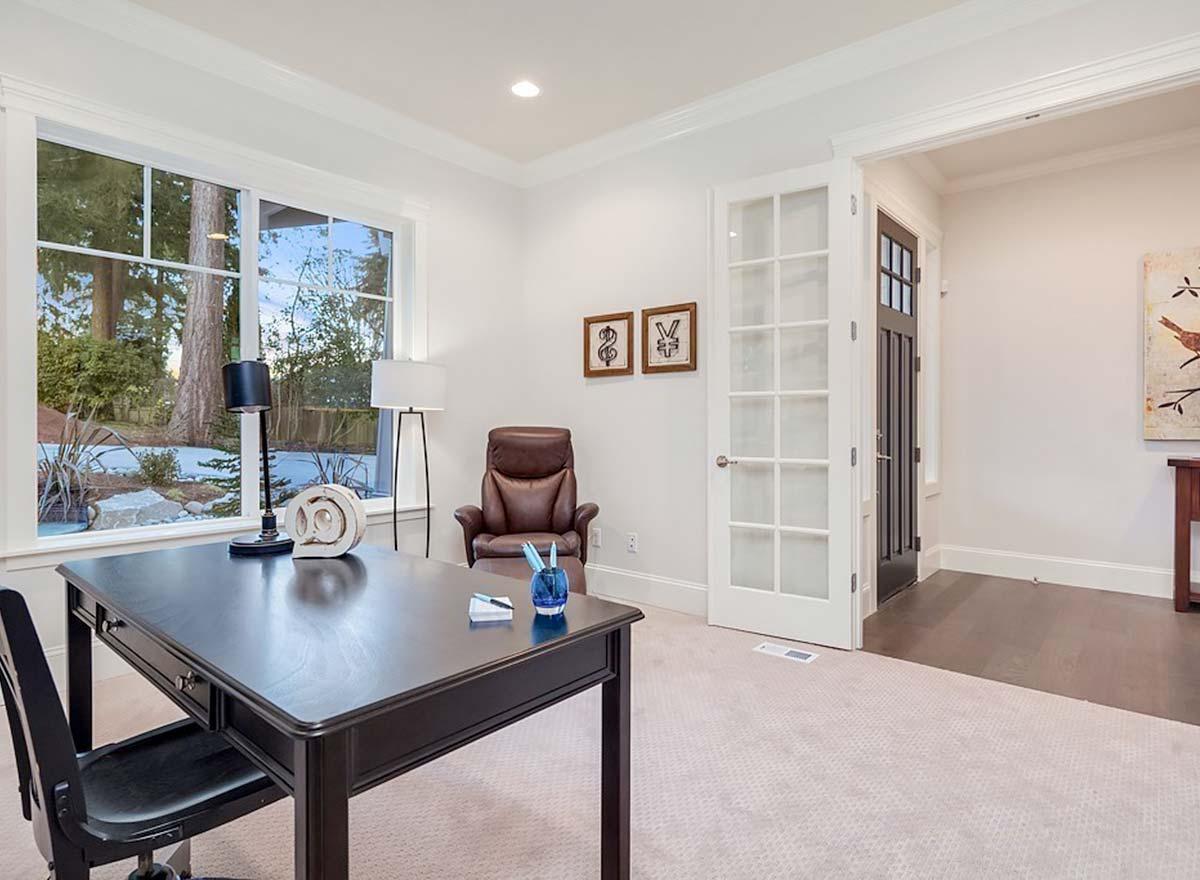 Home office with dark desk, leather chair, and large window overlooking trees. French doors open to a hallway.