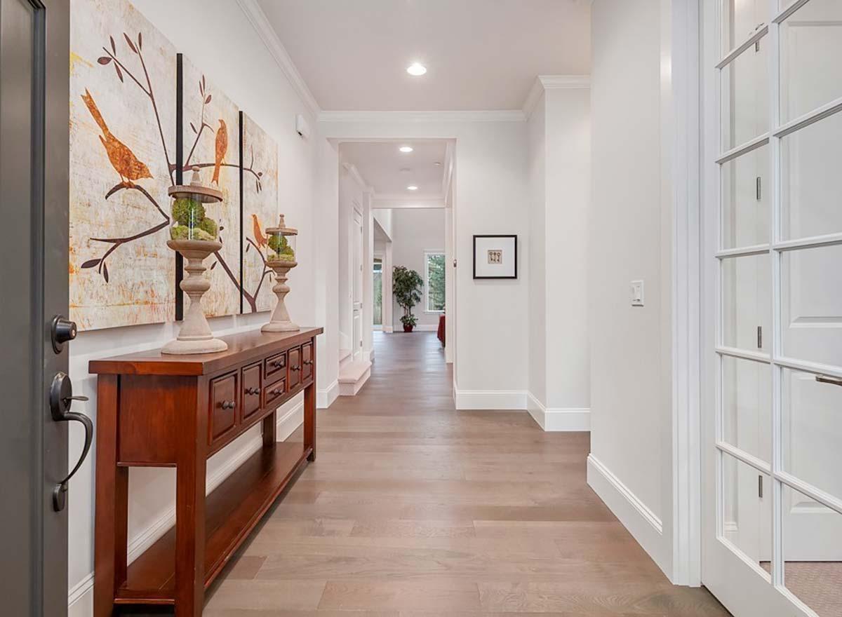 Interior view of a hallway with hardwood floors, a console table, and art. Double doors visible on the right.