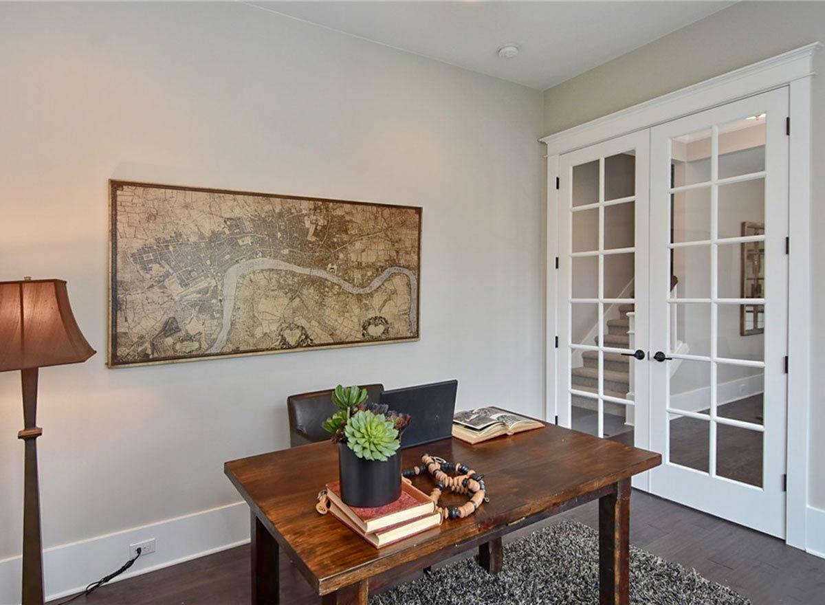 Home office with a wooden desk, vintage map art, and double glass-paned doors revealing a staircase.