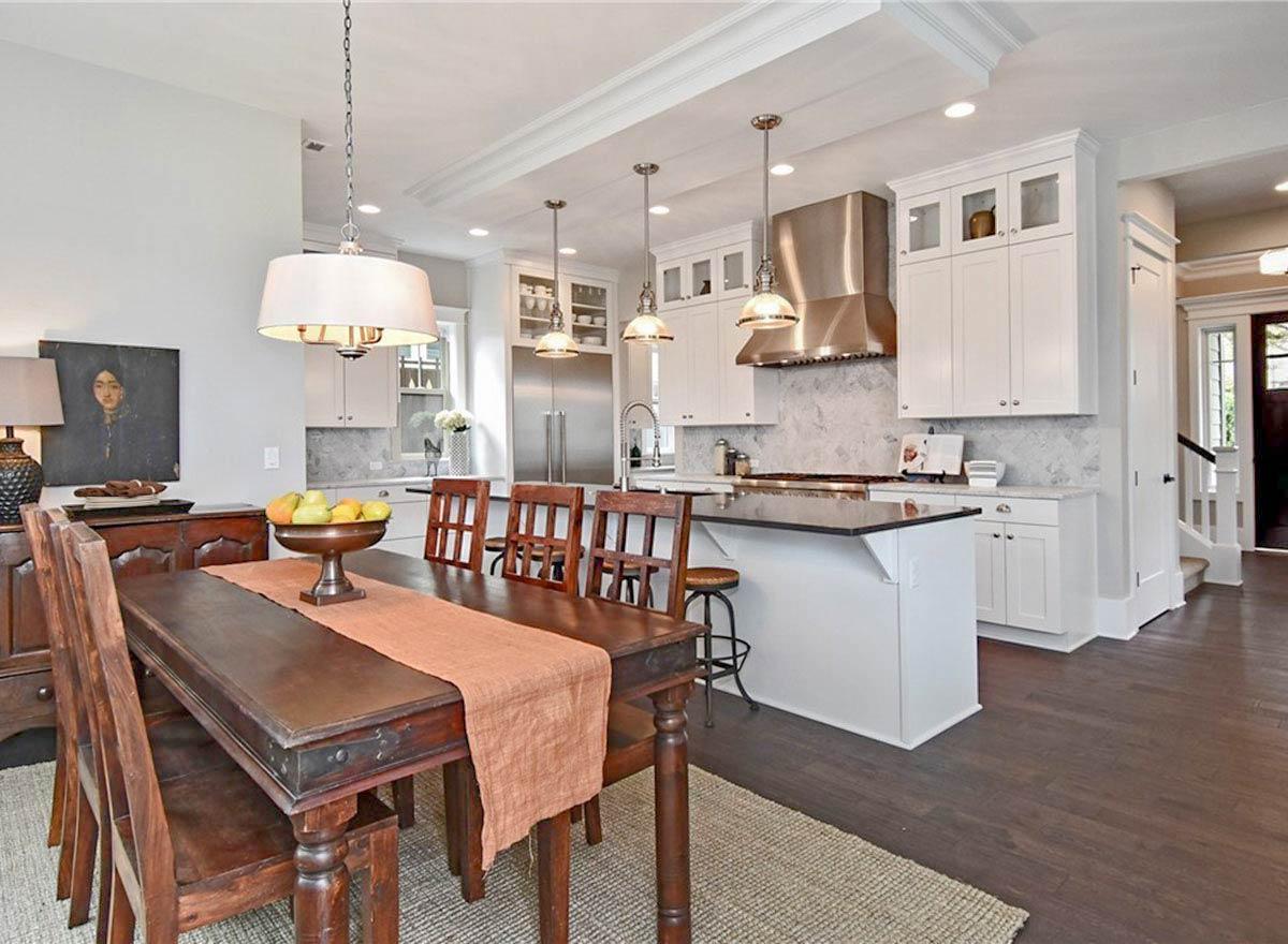Interior view of a kitchen and dining area with white cabinets, a large island with seating, and stainless steel appliances.