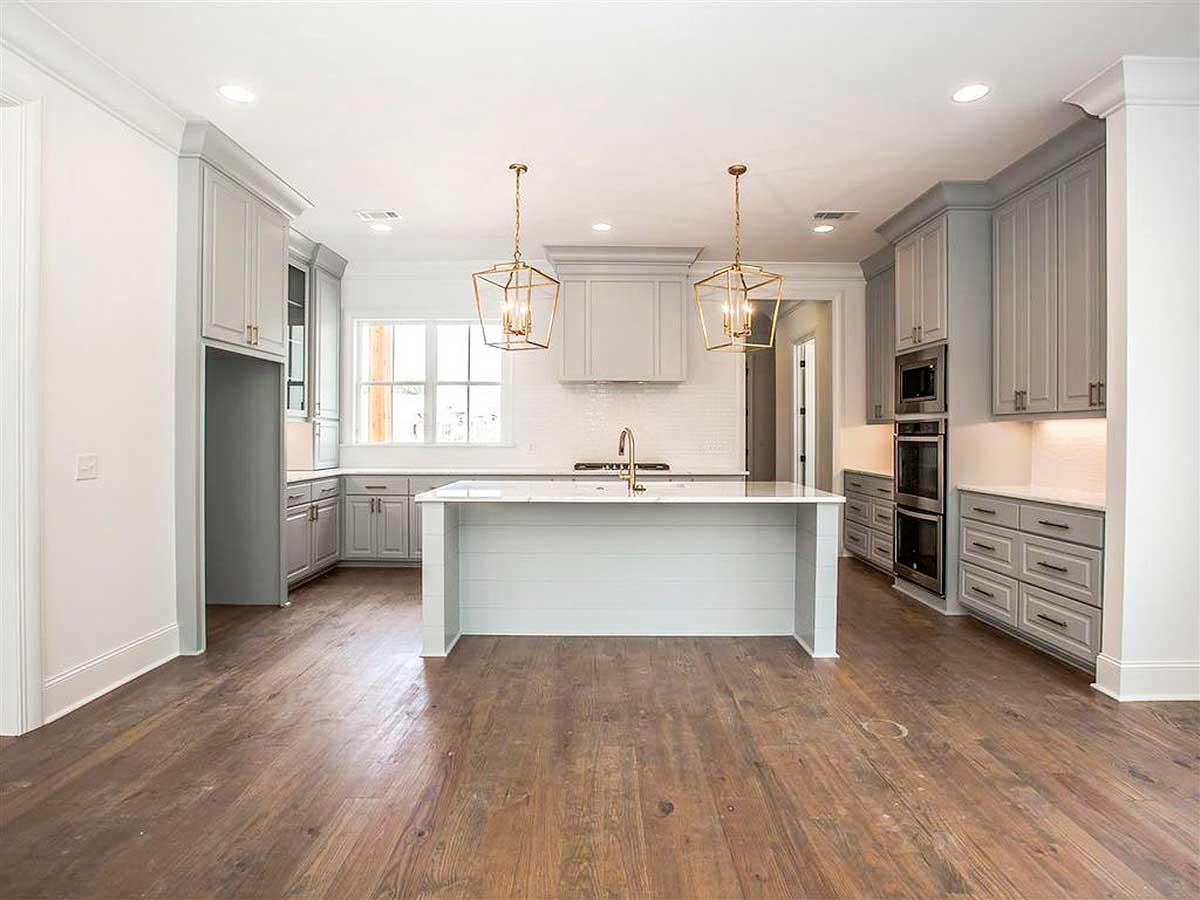 Kitchen with gray cabinets, large island with white countertop, built-in double oven, and pendant lights.