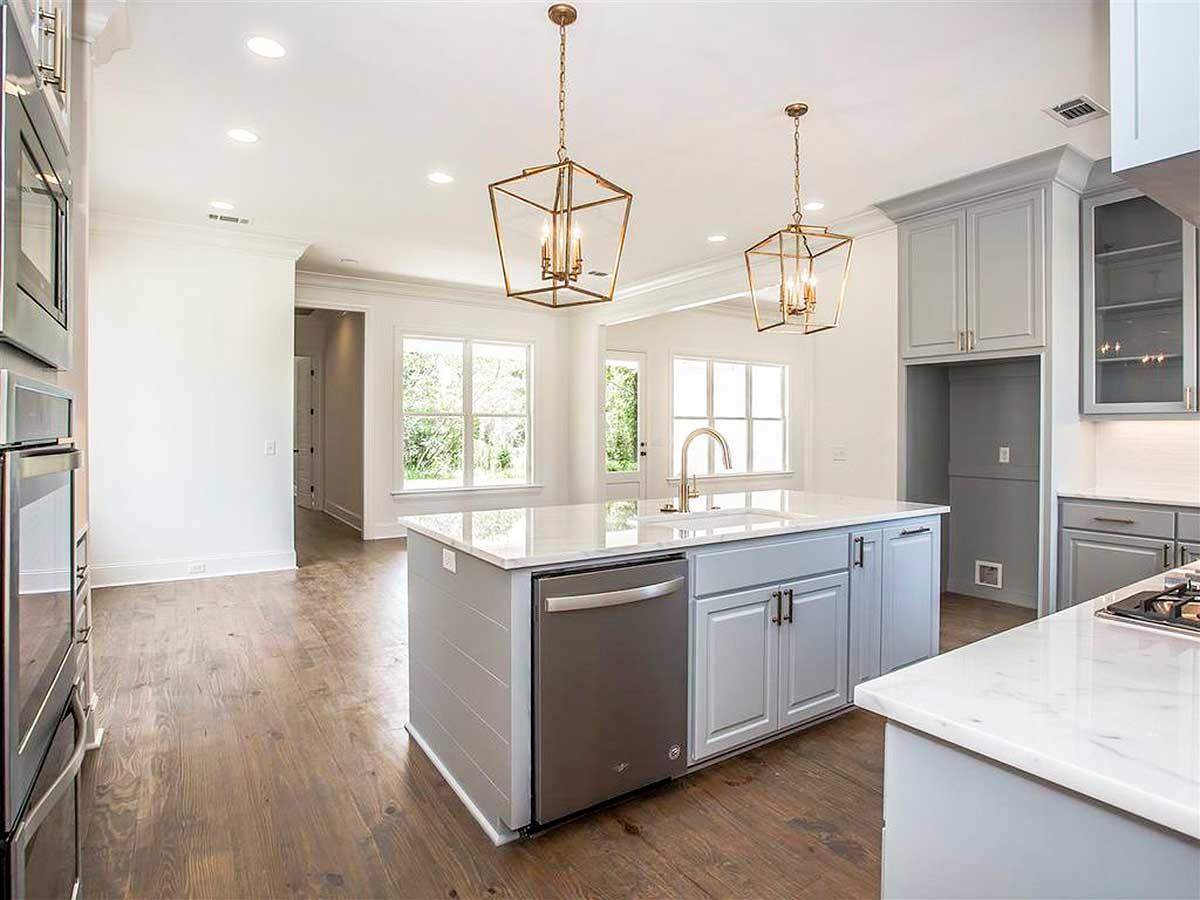 Kitchen with gray island, white countertops, stainless steel dishwasher, and two gold geometric pendant lights.
