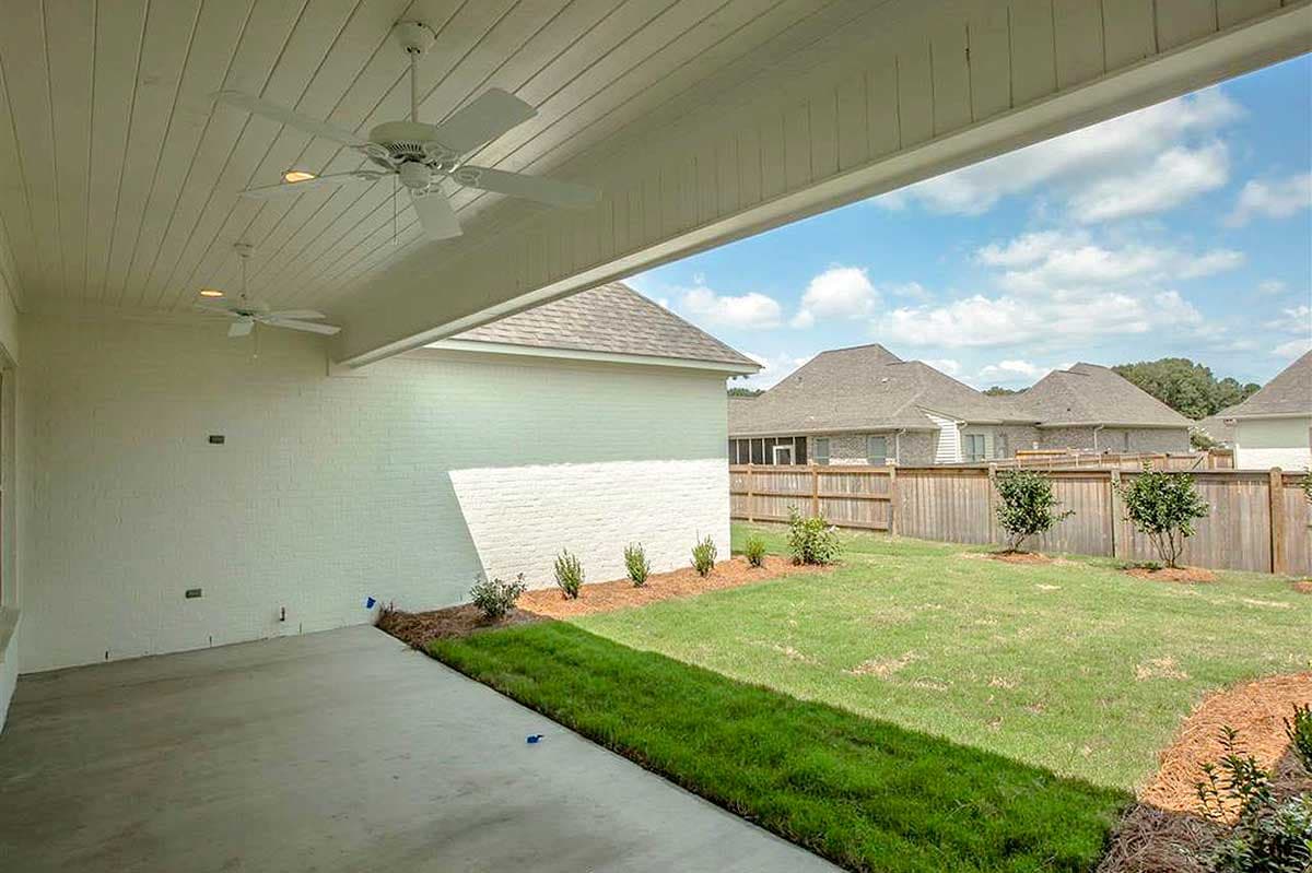 Covered patio with ceiling fans overlooks a backyard with a wooden fence and landscaping.
