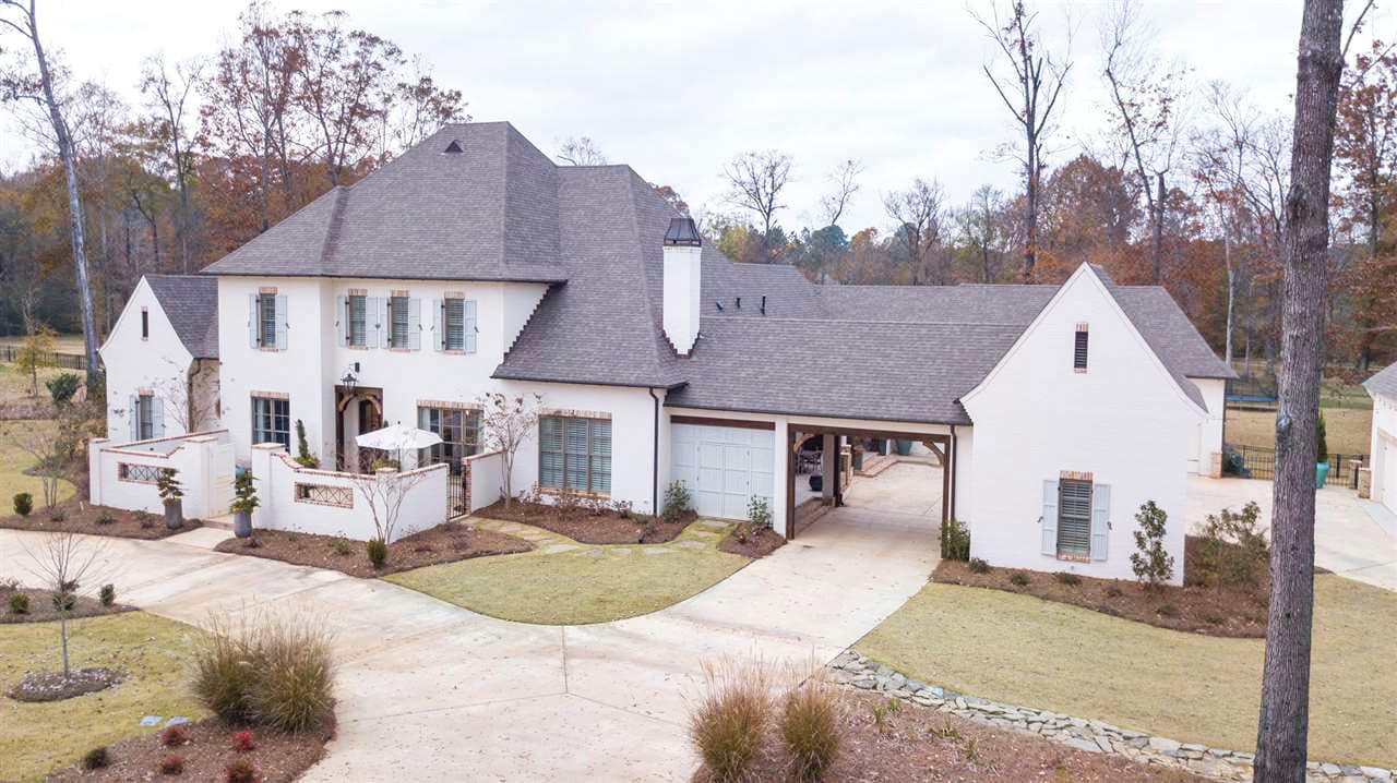House plan exterior: Two-story white stucco home with gables, dormers, white brick accents, and a porte-cochere.