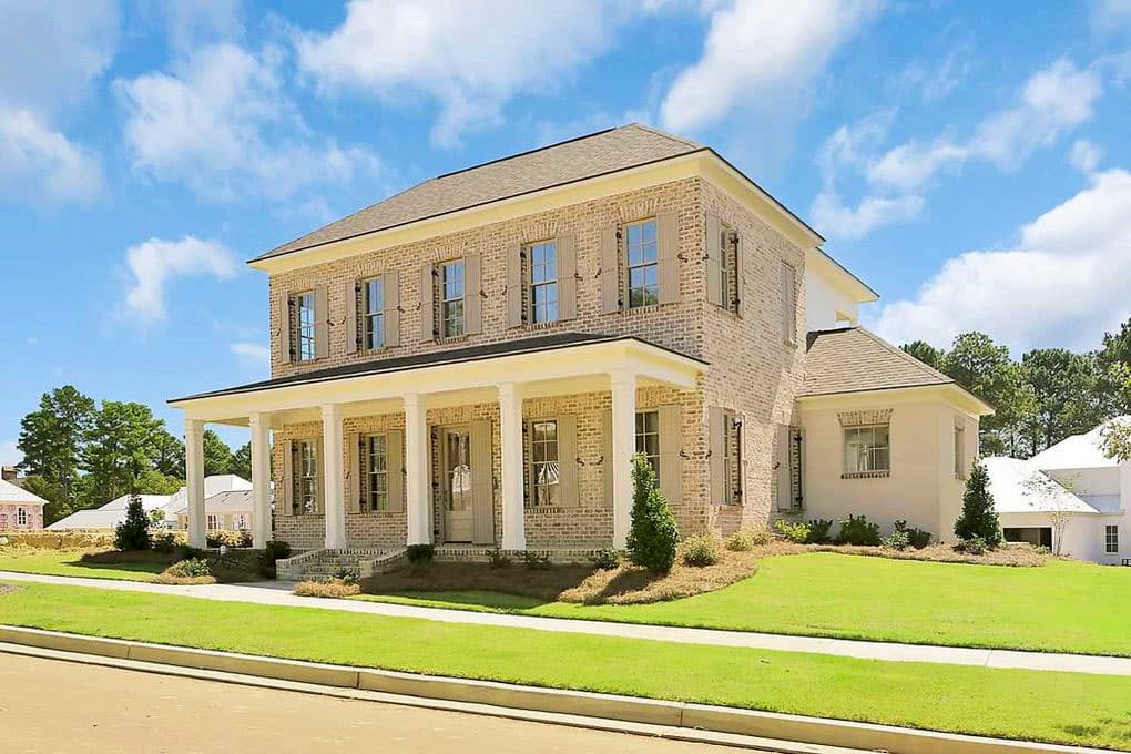 House plan exterior. Two-story home with columns supporting a front porch. Features include dormers, brick facade, and a hipped roof.