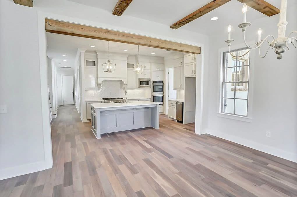 Interior view of a kitchen with island, dual ovens, range, and decorative range hood, featuring exposed wooden ceiling beams.