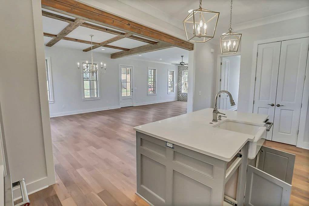 Kitchen island with sink, open great room with coffered wood beam ceiling, and a brick fireplace.