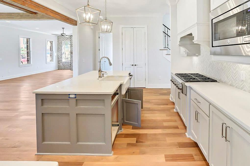 Kitchen island with sink, gas range, and microwave integrated into white cabinetry with white tile backsplash.
