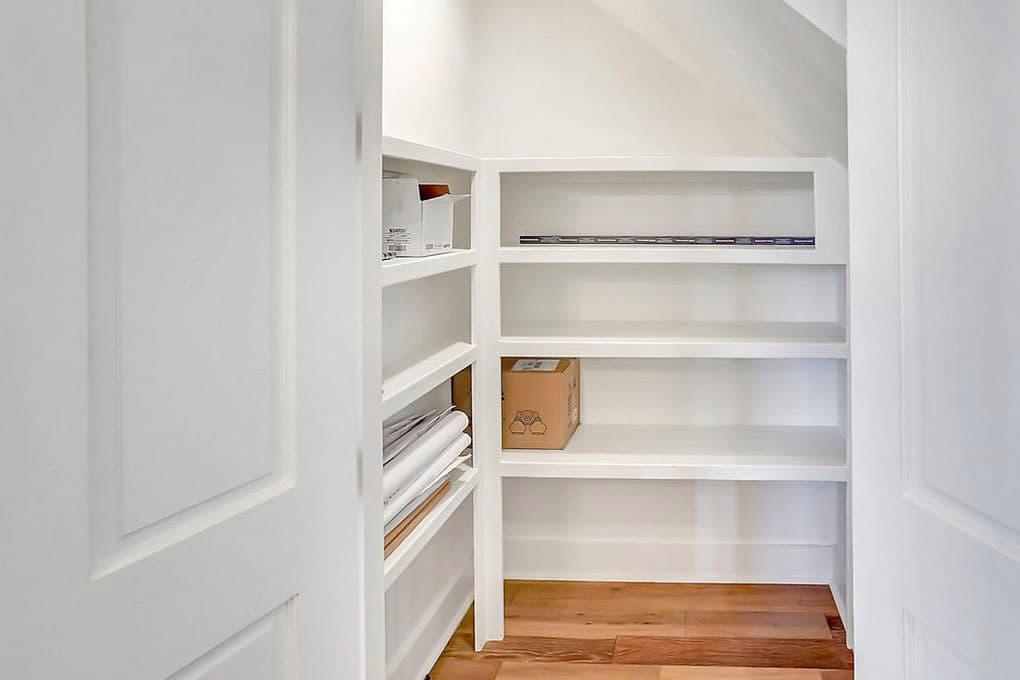 Interior view of a white closet with built-in shelves containing boxes and folded papers, hardwood floor.