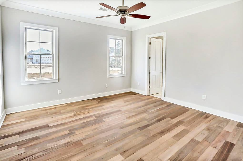 Interior view of a room with light gray walls, wooden plank flooring, a ceiling fan, and two windows.