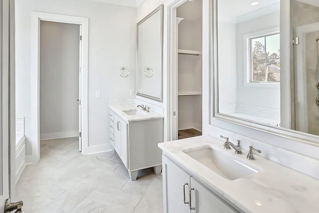 Bathroom interior with dual vanities, marble countertops, walk-in closet, and tiled tub/shower area.