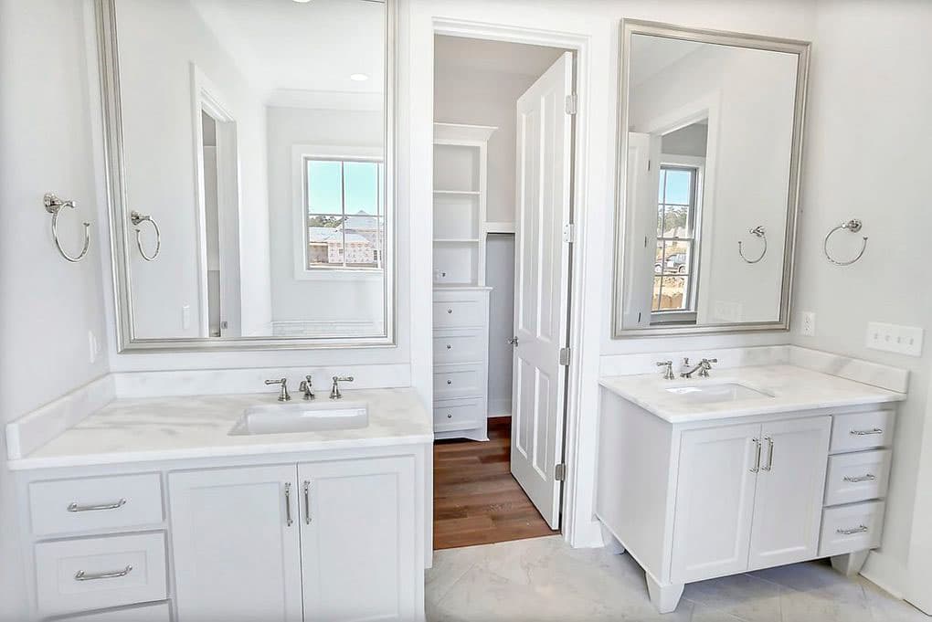 Bathroom with double vanity, marble countertops, and an open closet with shelving and drawers.
