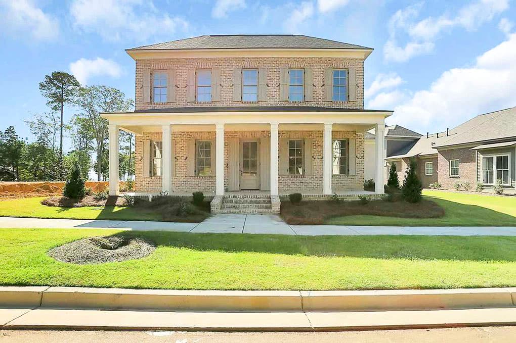 Two-story brick house plan with wide covered front porch, double-hung windows with shutters, and brick steps.