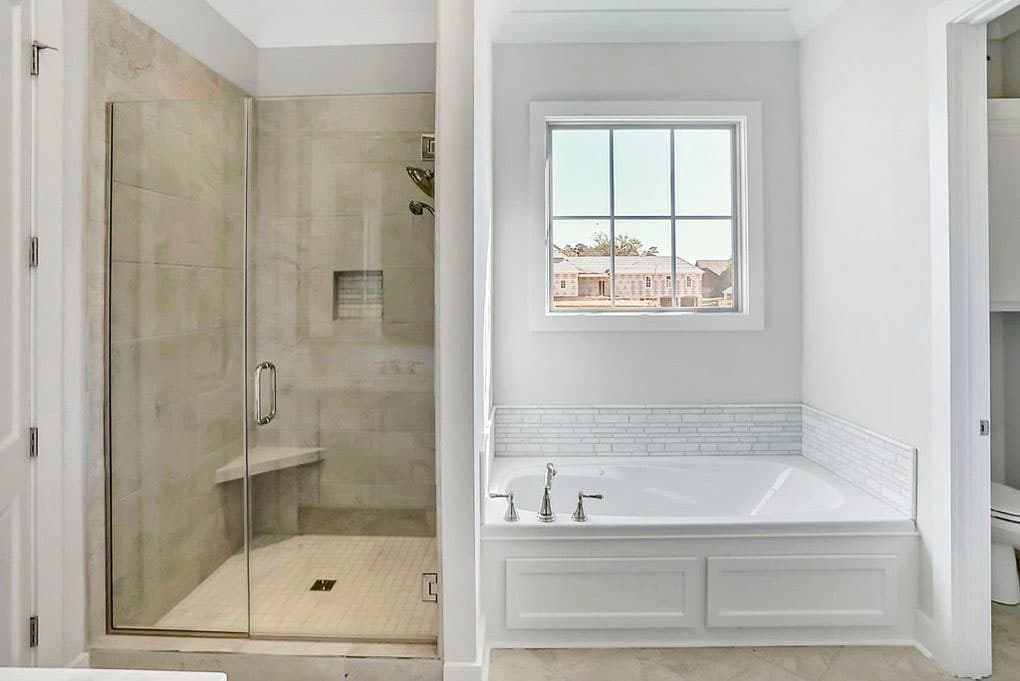 Bathroom with glass-enclosed tiled shower, soaking tub with subway tile backsplash, and window view of exterior construction.