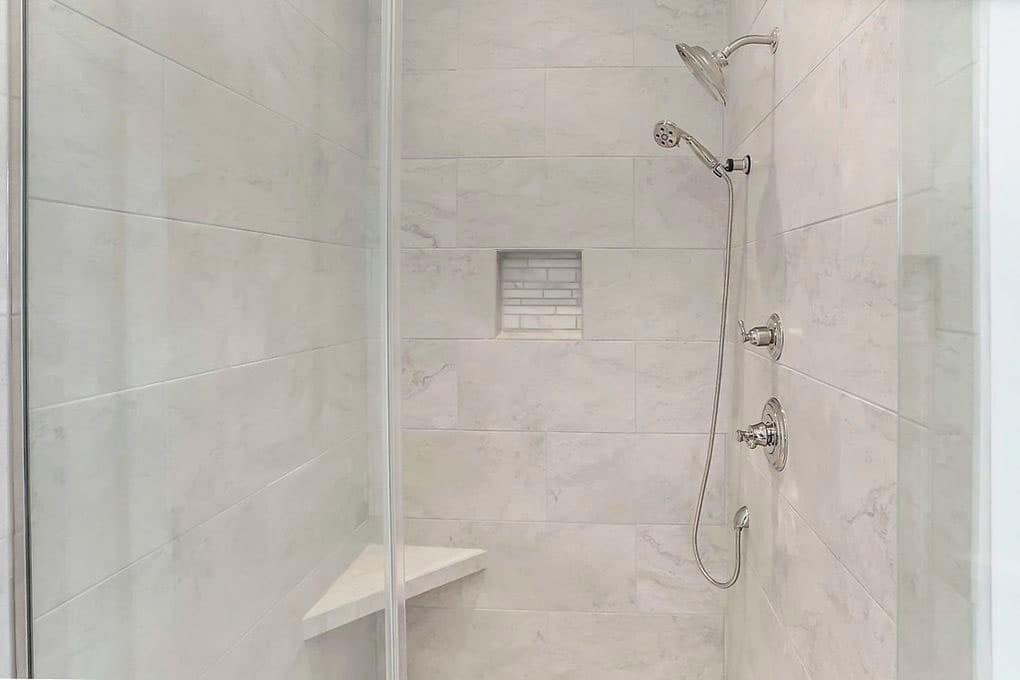 Shower with marble tile, dual showerheads, built-in niche, and corner bench seat.