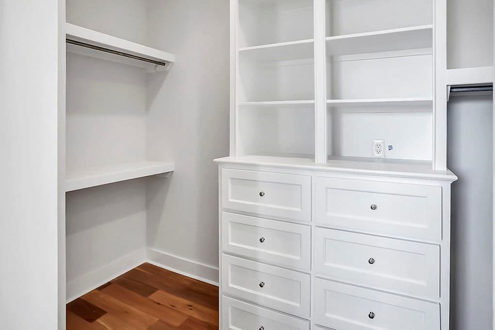 Walk-in closet with white built-in shelving, drawers, and rod. Hardwood floor visible.