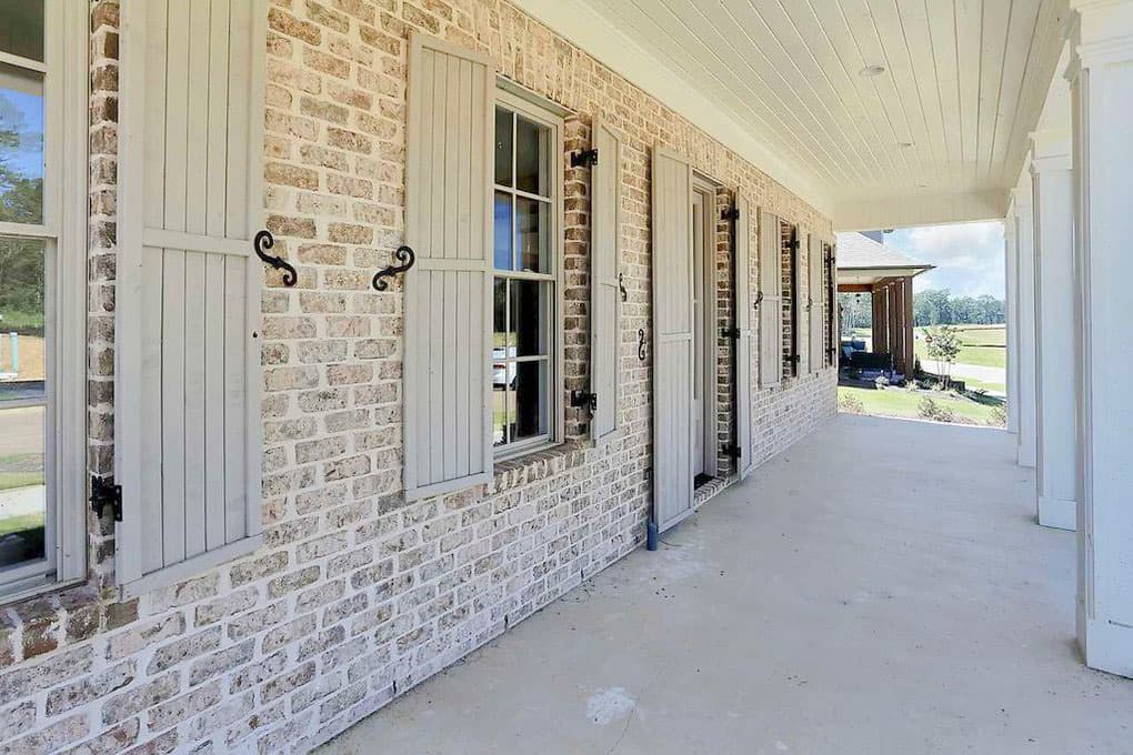 House plan exterior with brick facade, louvered shutters, and covered porch with columns.