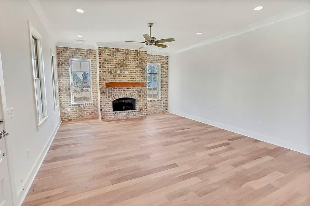 Interior view of a room with a brick fireplace, wood mantel, ceiling fan, and hardwood floors.