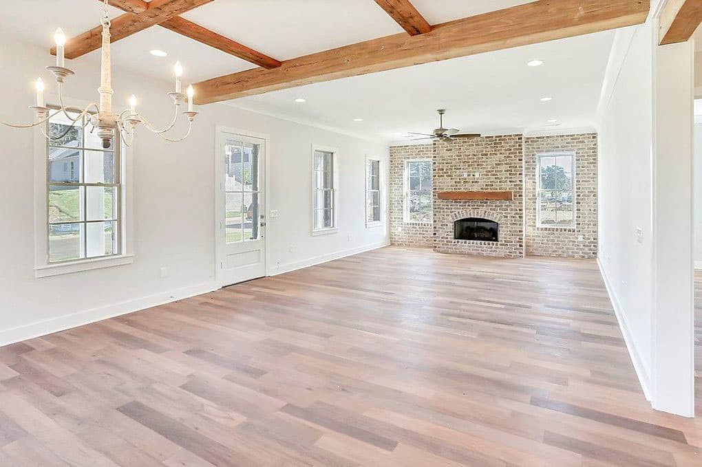 Interior rendering of an open-concept great room with exposed wooden beams, a brick fireplace, and hardwood floors.