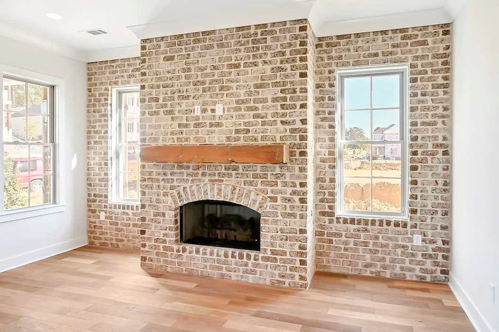Interior view of a room with a floor-to-ceiling brick fireplace, wood mantel, arched firebox, and casement windows.