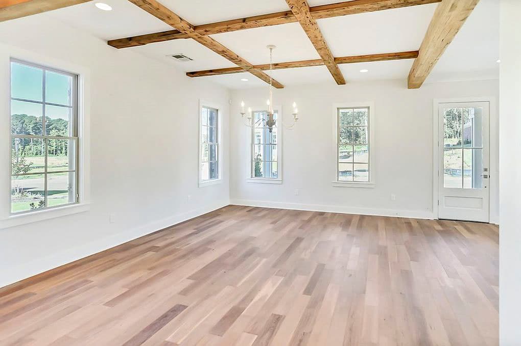 Interior rendering of an open room with coffered wood beam ceiling, hardwood floors, multiple windows, and a glass door.