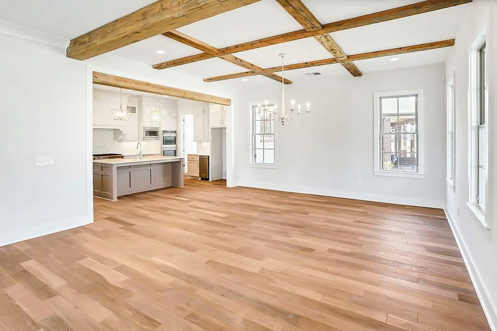 Open concept living area and kitchen with coffered wood beam ceiling, kitchen island with seating, and wood flooring.