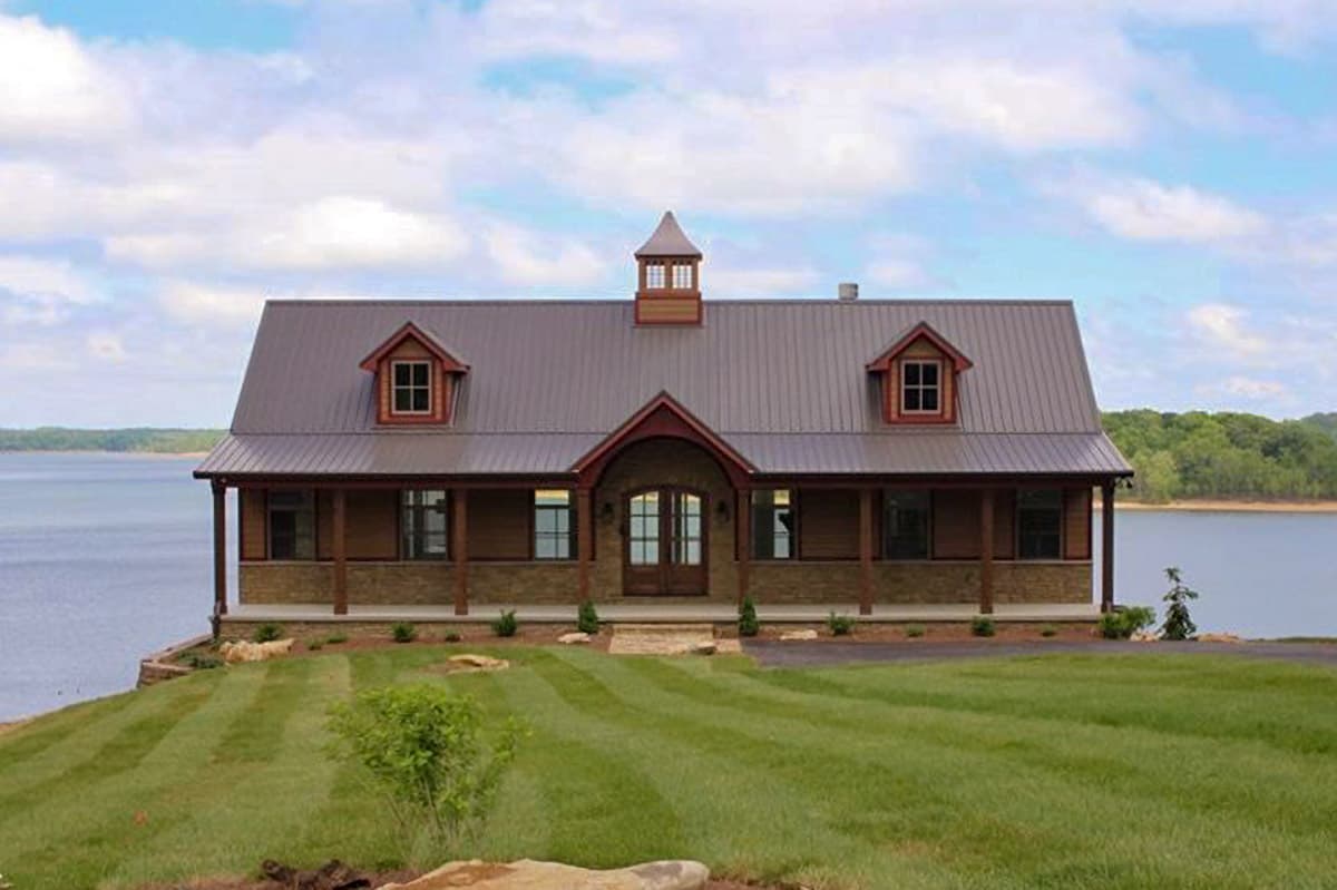 House plan exterior with metal roof, two dormers, covered porch, and cupola. Craftsman style home plan on a lakefront property.