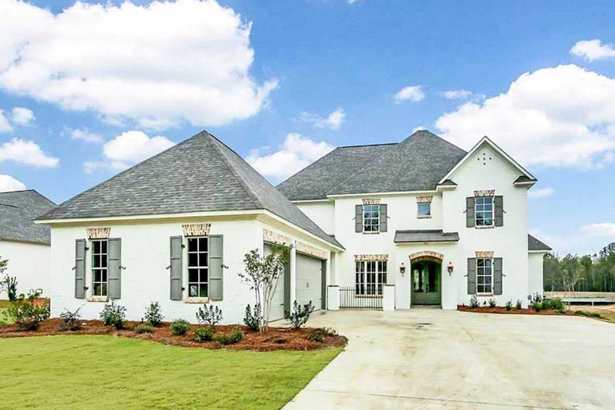 House plan exterior. Two-story house in a French Provincial style. Features include multiple gabled roofs, shutters, and an attached garage.
