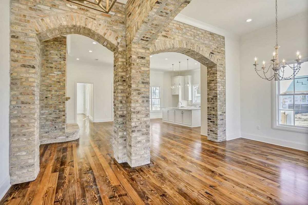 Interior view of open-concept living space with exposed brick archways, wood floors, and view of kitchen.