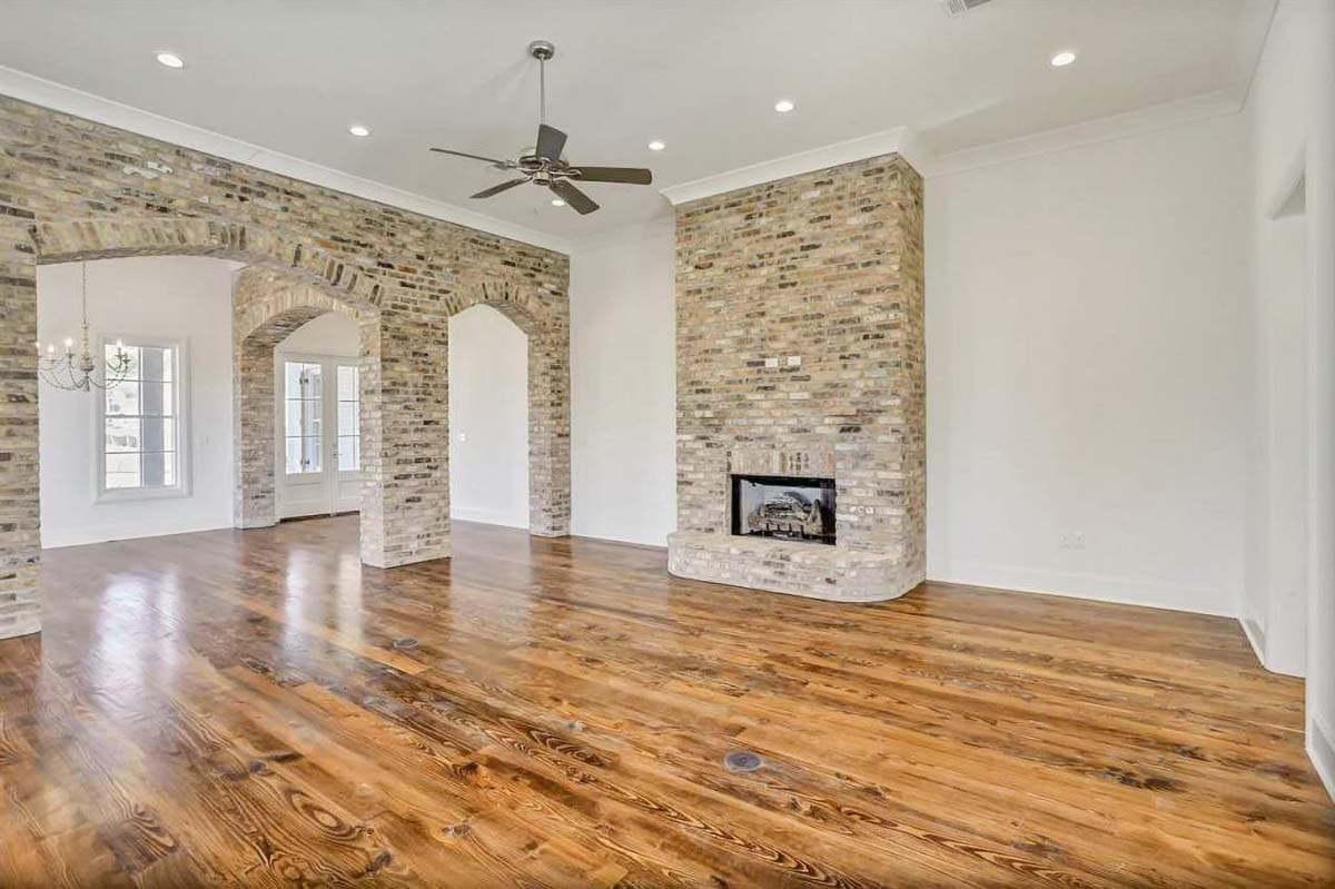 Interior view of a great room with exposed brick fireplace, arched entryways, wooden floors, and a ceiling fan.