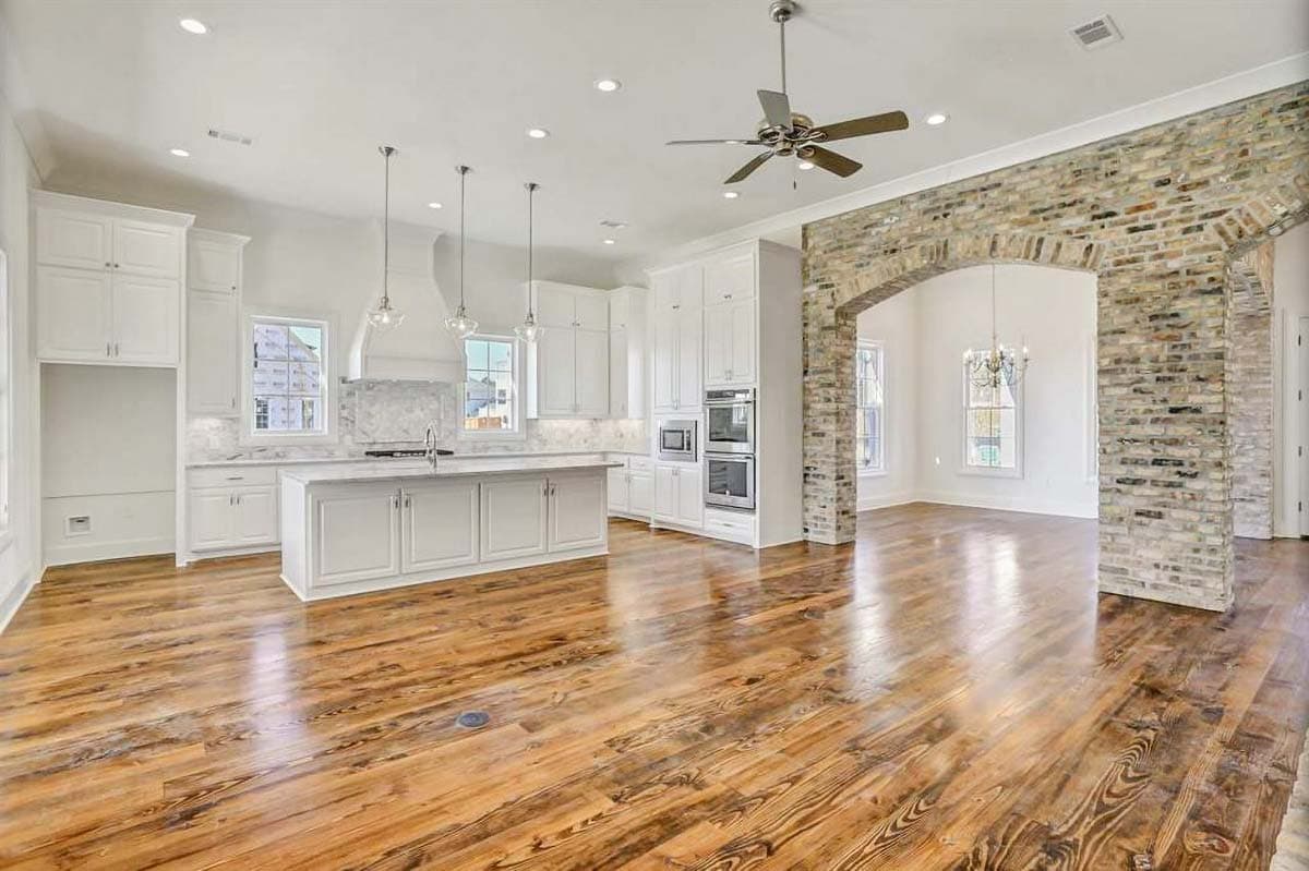 Open concept interior with kitchen island, white cabinetry, brick archway, and wood floors.