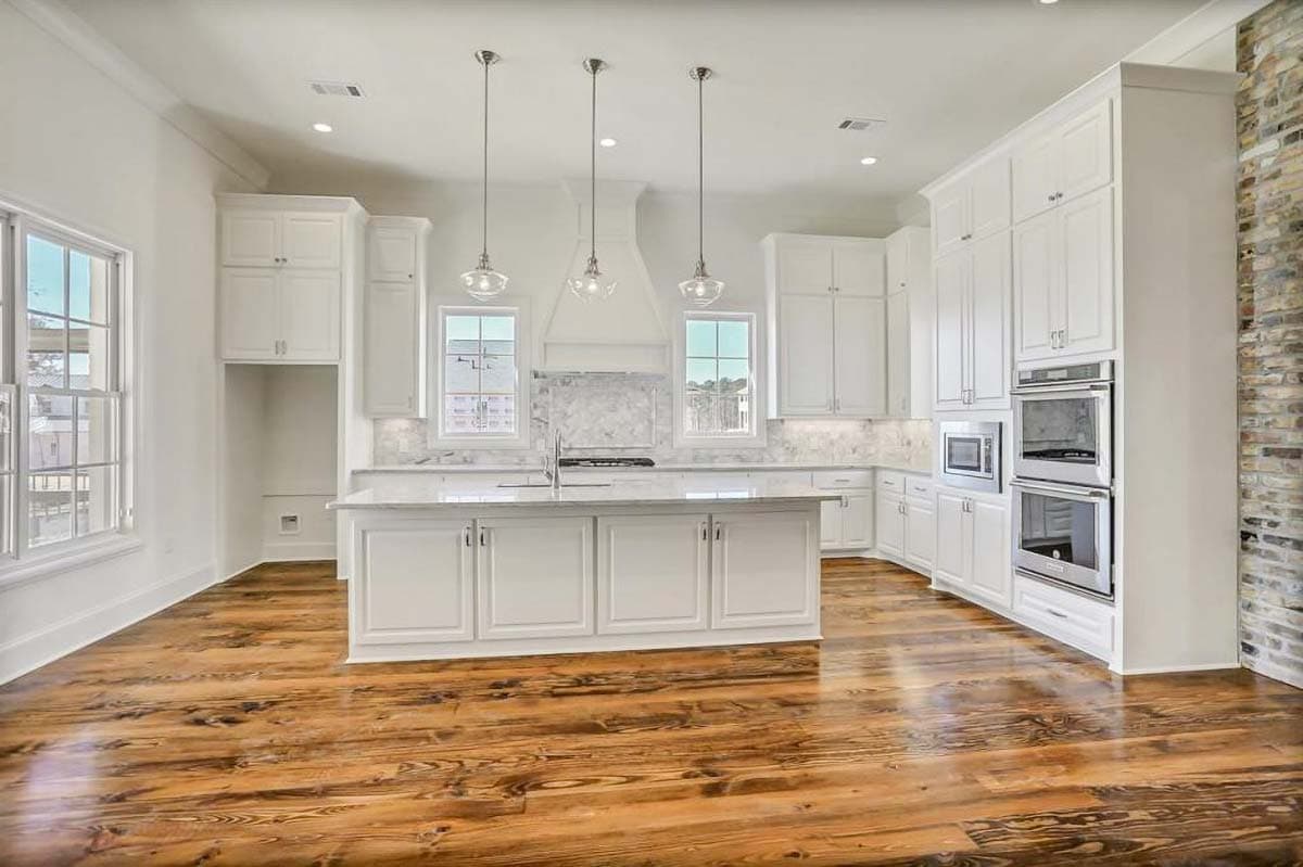 Kitchen interior with white cabinetry, a central island with sink, marble backsplash, stainless steel appliances, and hardwood floors.