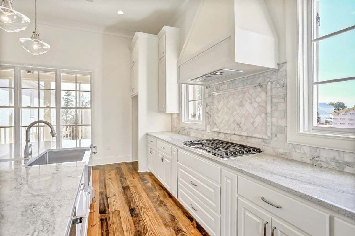 Kitchen featuring white cabinets, marble countertops and backsplash, gas range, stainless steel sink, and wood flooring.