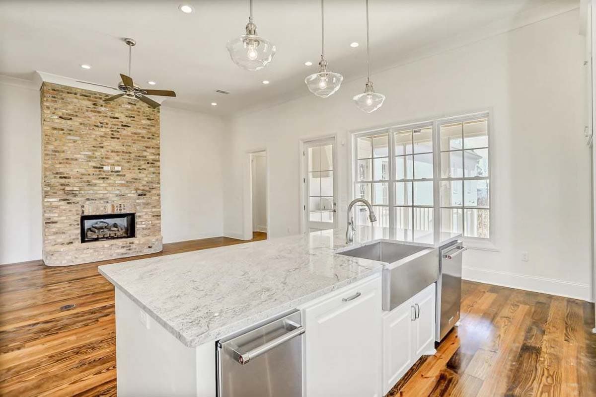 Interior view of a modern farmhouse kitchen with a large island, farmhouse sink, stainless steel appliances, and a brick fireplace.