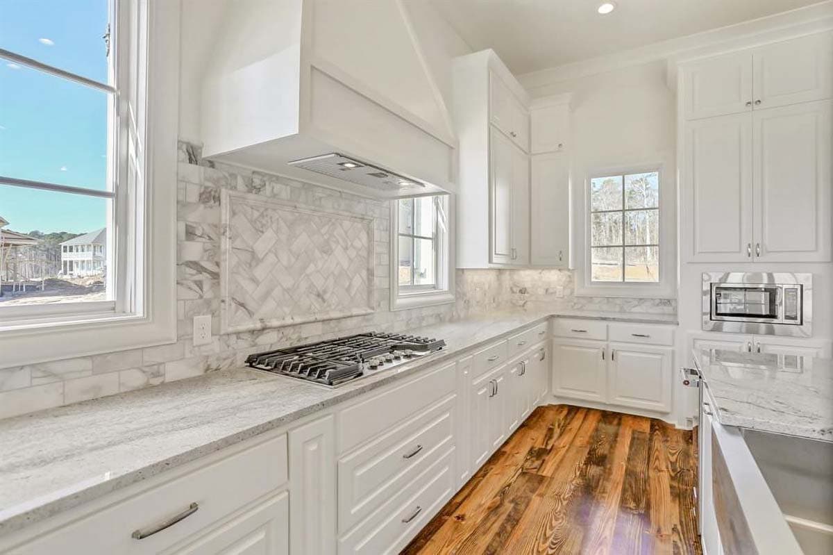 Kitchen with white cabinets, gas range, marble backsplash, granite countertops, and wood floors.