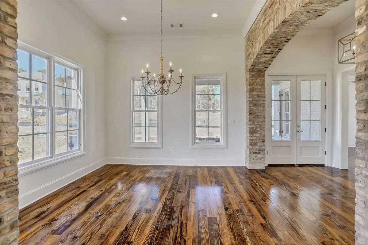 Interior view of a dining room featuring a brick arched entryway, chandelier, and large windows overlooking new construction.
