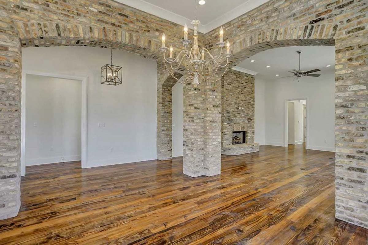 Interior view of a living area with arched brickwork, a stone fireplace, hardwood floors, and a chandelier.