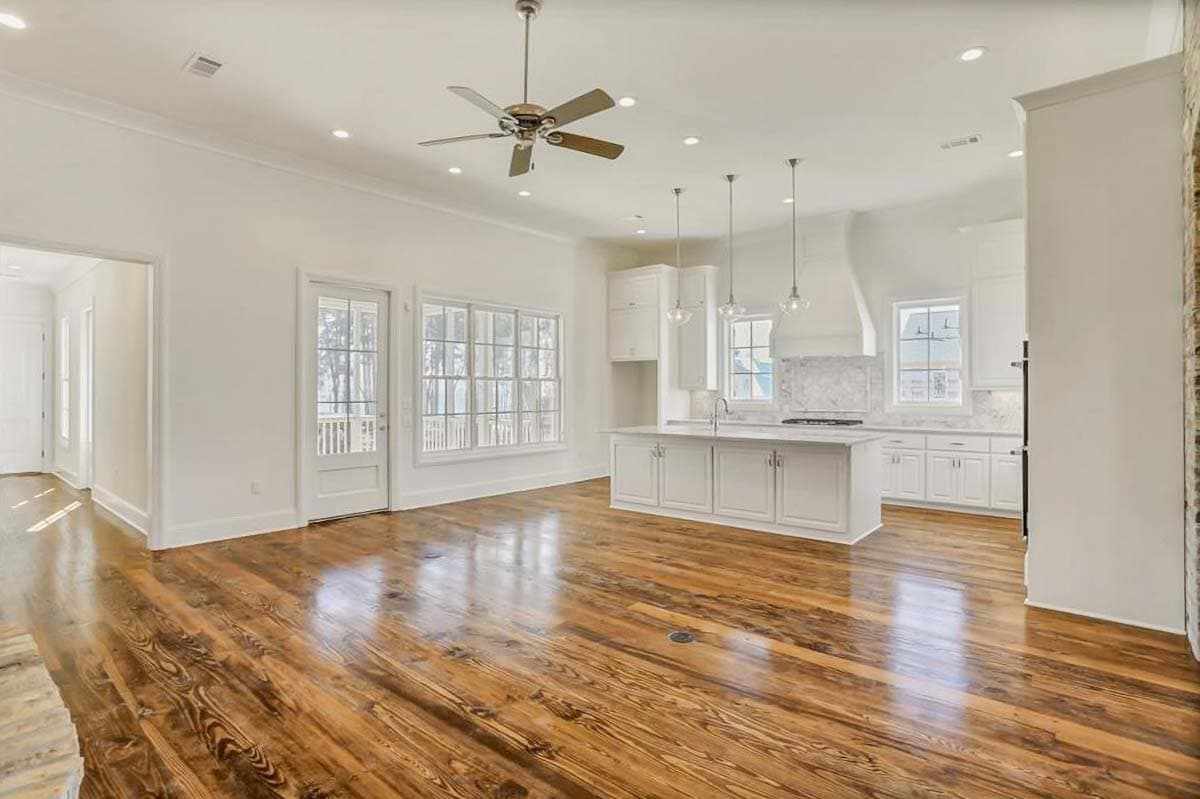 Interior view of a home featuring an open-concept living and kitchen area with a central island, white cabinetry, and large windows.