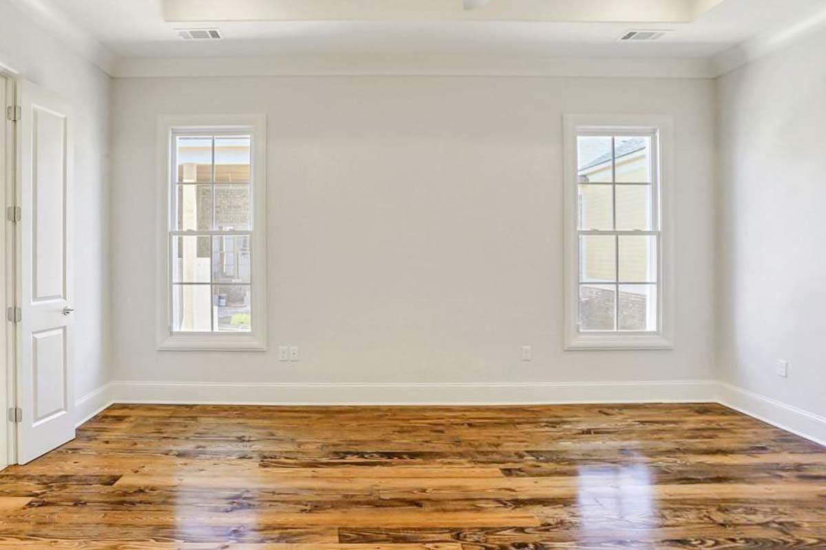 Interior view of a room with hardwood floors, two double-hung windows, and a white paneled door.