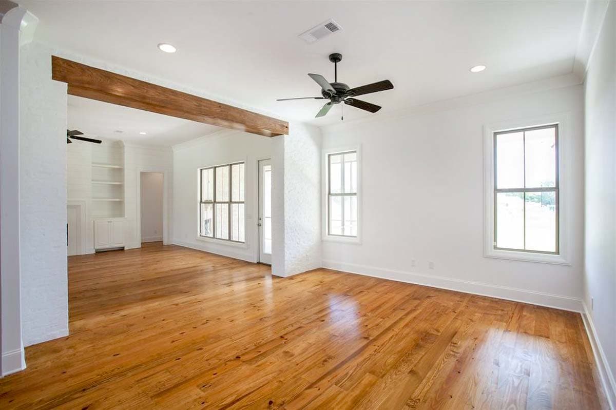 Interior rendering of an open-concept living area with exposed wooden beams, ceiling fan, and large windows.