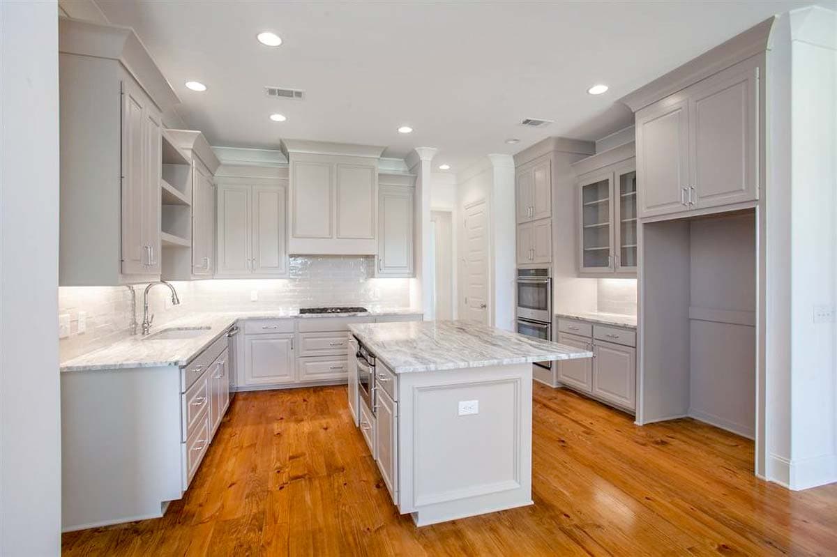 Kitchen with gray cabinets, white marble countertops, central island, double oven, and hardwood floors.