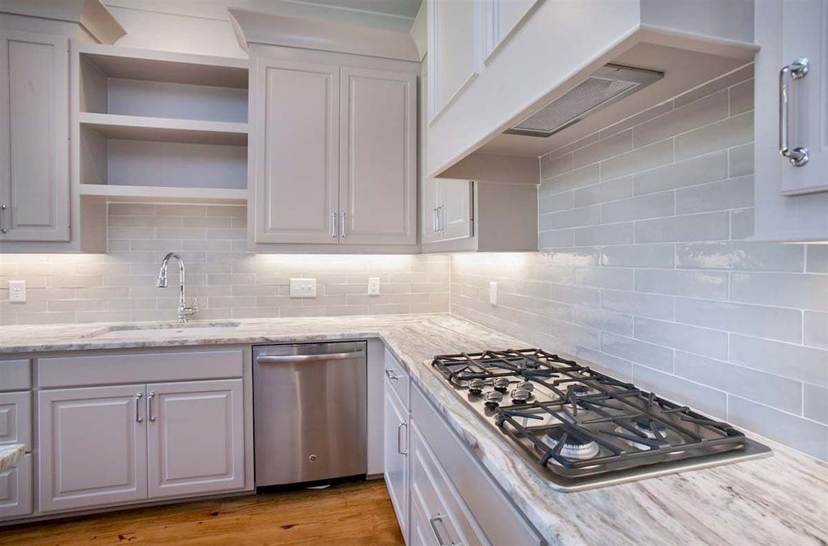 Kitchen with gray cabinets, subway tile backsplash, stainless steel dishwasher, and gas range on marble countertop.