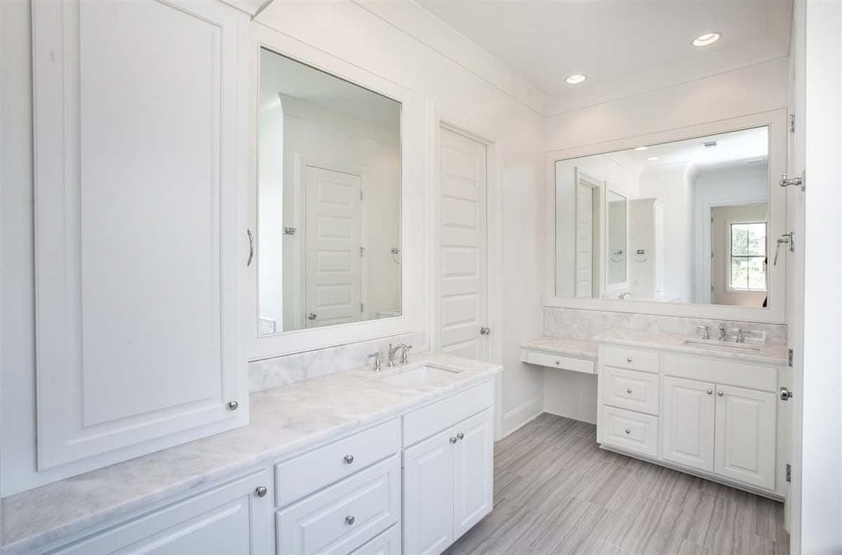 Bathroom interior with double vanity, marble countertops, built-in cabinets, and gray wood-look tile flooring.