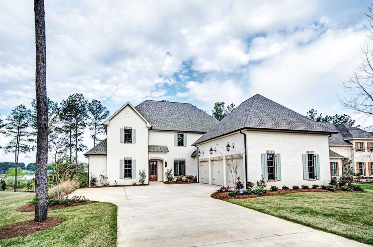 House plan exterior: Two-story brick home with a front-facing three-car garage, prominent gables, and decorative shutters.
