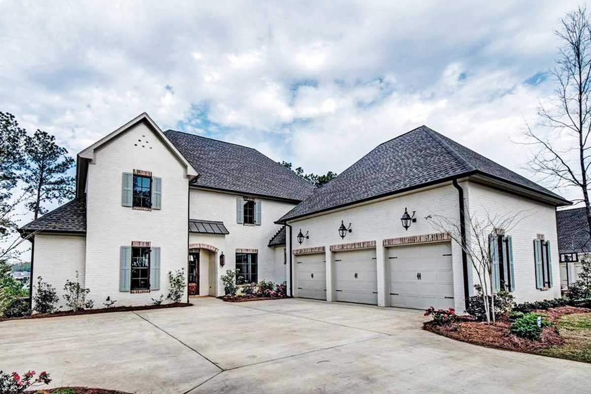 House plan exterior. Two-story home with a gabled roof, brick accents, and a three-car garage. Shutters and entryway awning are visible.