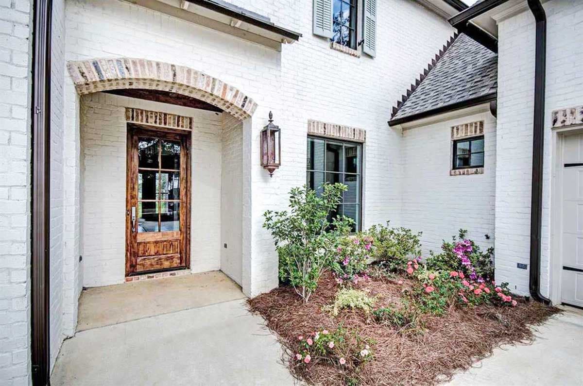 House plan exterior with white brick, arched entryway, wood door, multi-story gables, and landscaping.